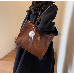 Détail d'un cabas marron avec pompon blanc et surpiqûres sur l'épaule d'un mannequin