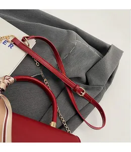 Close-up of red leather handbag featuring gold chain and decorative silk scarf handle