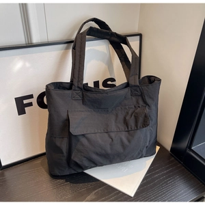 Detail of black nylon tote bag featuring front flap pocket and wide carry handles