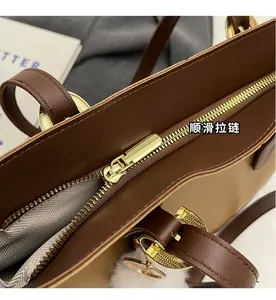Close-up of smooth gold zipper and texture of large brown tote bag with fuzzy charm