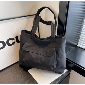 Detail of a large black nylon tote bag with functional front flap pocket and sturdy straps