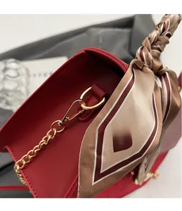 Detail of red PU leather bag with golden metal hook and striped silk scarf wrap