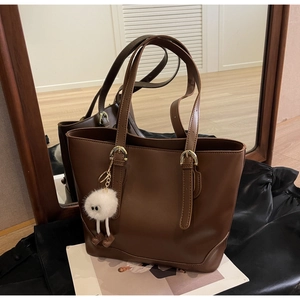 Detail of dark brown leather tote bag with white plush charm and gold hardware accents