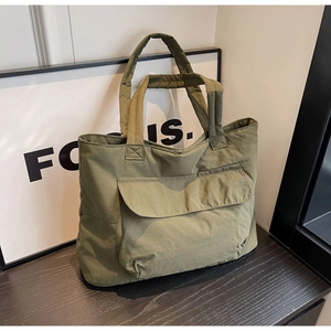 Detail of army green nylon tote bag featuring a large front flap pocket and wide handle