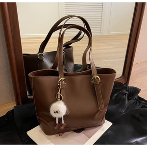 Close-up of brown PU leather tote bag featuring a cute white plush monster pendant