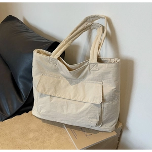 Detail of minimalist beige nylon tote bag with front flap pocket on stone surface