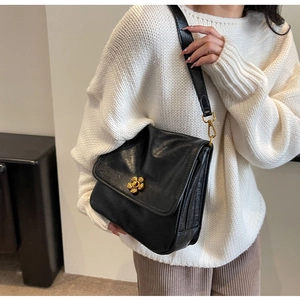 Close-up of black leather crossbody bag featuring a golden flower-shaped buckle on white sweater