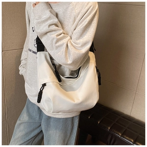 Detail of the white dumpling bag showing wide black shoulder strap and knot zipper