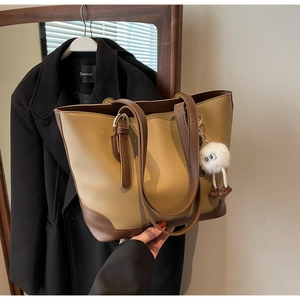 Detail of a large two-tone tote bag with a plush charm and brown leather straps