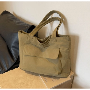Detail of khaki nylon tote bag featuring front pocket and reinforced handles on stone base