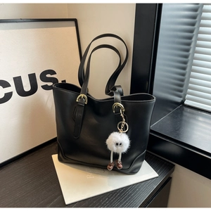 Detail of black tote bag with matte leather texture, gold hardware, and a plush charm