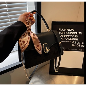 Detail of black crossbody bag with leather patchwork, gold clasp, and heart silk scarf