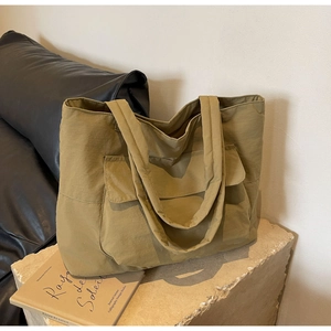 Detail of olive nylon tote bag with front pocket and wide strap on stone base