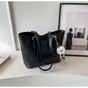 Close-up of black tote bag featuring golden hardware and a white plush monster charm