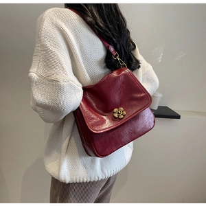 Close-up of vintage burgundy shoulder bag with an elegant golden flower lock on a white sweater