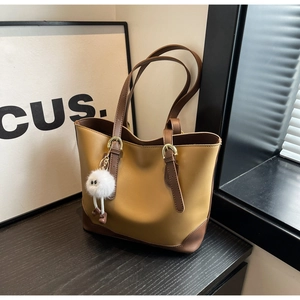 Close-up of khaki and brown tote bag with adjustable straps and plush monster charm