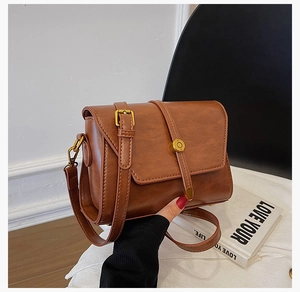 Détail d'un sac bandoulière en cuir PU marron caramel avec boucle dorée et rabat chic