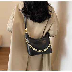 Close-up of black quilted shoulder bag with gold chain strap on a khaki trench coat
