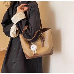 Detail of minimalist two-tone tote bag in brown leather with a cute plush monster charm