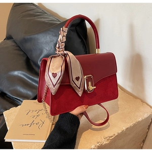 Detail view of red leather crossbody bag with metal clasp and scarf-wrapped handle