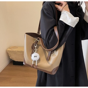 Detail of minimalist khaki and brown tote bag with fuzzy charm on shoulder strap