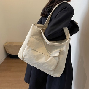Minimalist beige nylon tote bag with wide shoulder strap and front pocket worn by a model