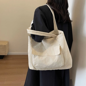 Minimalist nylon tote bag in cream white with front pocket shown on shoulder