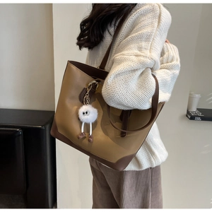 Detail of the large faux leather tote bag in camel and dark brown with a plush charm