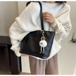 Detail view of large black minimalist tote bag with a white plush pompom charm