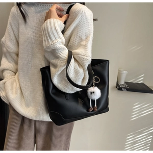 Close-up of black leather tote bag featuring a cute white plush doll pendant detail