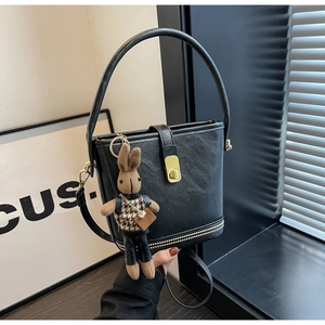 Gros plan du sac seau noir mat avec détails dorés et breloque lapin en peluche mignonne
