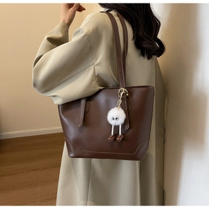 Detailed side view of large brown tote bag with fuzzy charm and slim straps