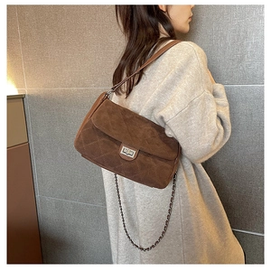 Detailed view of quilted dark brown suede handbag with silver turn-lock on a model