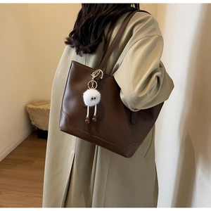 Detail view of coffee brown leather tote bag with plush monster charm for commuting