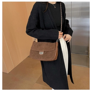 Detail of a brown quilted suede shoulder bag with chain strap and metal swivel lock