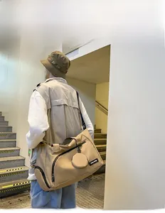 Große khakifarbene Reisetasche an männlichem Model mit kleinem runden Anhängetäschchen