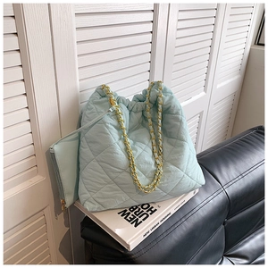 Détail du sac seau matelassé bleu clair avec chaîne dorée sur un canapé en cuir noir