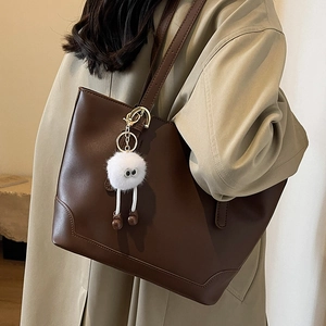 Minimalist large brown leather tote bag for women with a playful plush monster charm