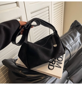 Dettaglio borsa a cuscino nera smerigliata con ampia tracolla su sfondo di libri di moda