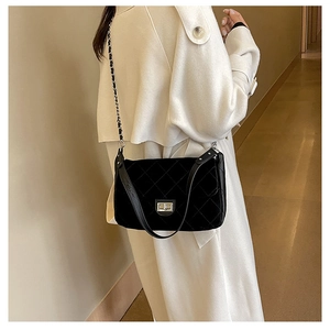 Close-up of black quilted suede shoulder bag with silver turn-lock and chain strap detail