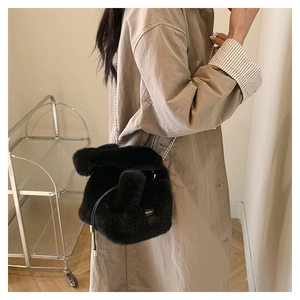 Close-up of black fuzzy bucket bag with silver chain strap worn by a model