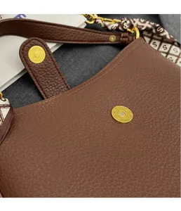 Macro detail of brown pebble grain leather bag with gold magnetic buckle and silk scarf