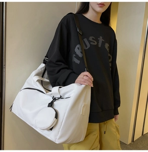 Details der weißen Reisetasche mit schwarzem Gurt und kleinem runden Münzbeutel-Anhänger