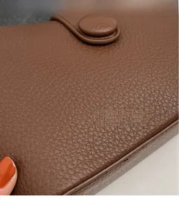 Close-up of brown pebbled grain leather texture and round buckle on a crossbody bag