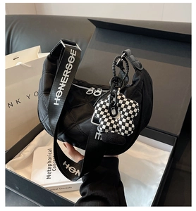 Détail du sac hobo en nylon matelassé noir avec bandoulière lettrée et breloque fleurie