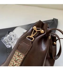 Detail of dark brown leather bucket bag featuring gold hardware and wavy woven shoulder strap