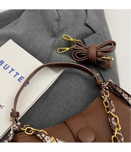 Detail view of brown pebbled leather handbag with silk scarf handle and gold chain hardware