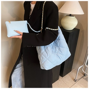 Détail d'un sac cabas matelassé bleu clair avec chaîne dorée porté par un mannequin