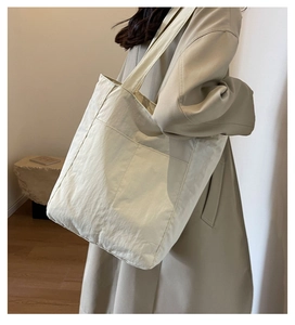 Macro side view of a large beige nylon tote bag worn with a stylish trench coat