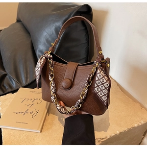 Detail of brown litchi pattern leather handbag with gold chain and silk scarf